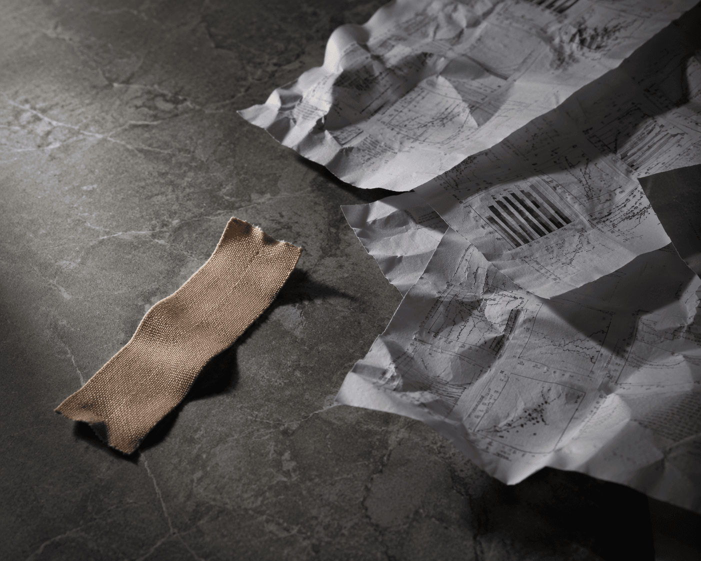 A torn strip of beige medical tape lying on a dark stone surface with scattered research papers nearby