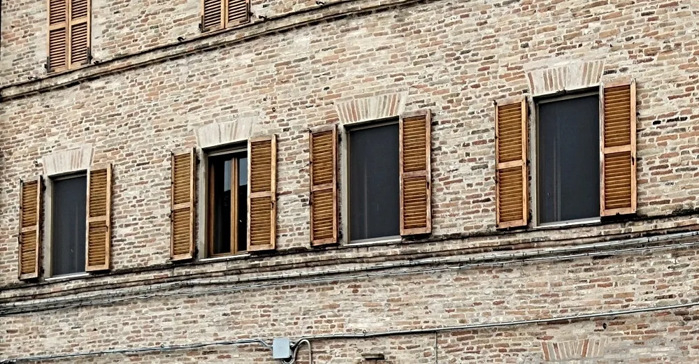 Traditional Italian stone building with closed wooden external shutters blocking summer sun