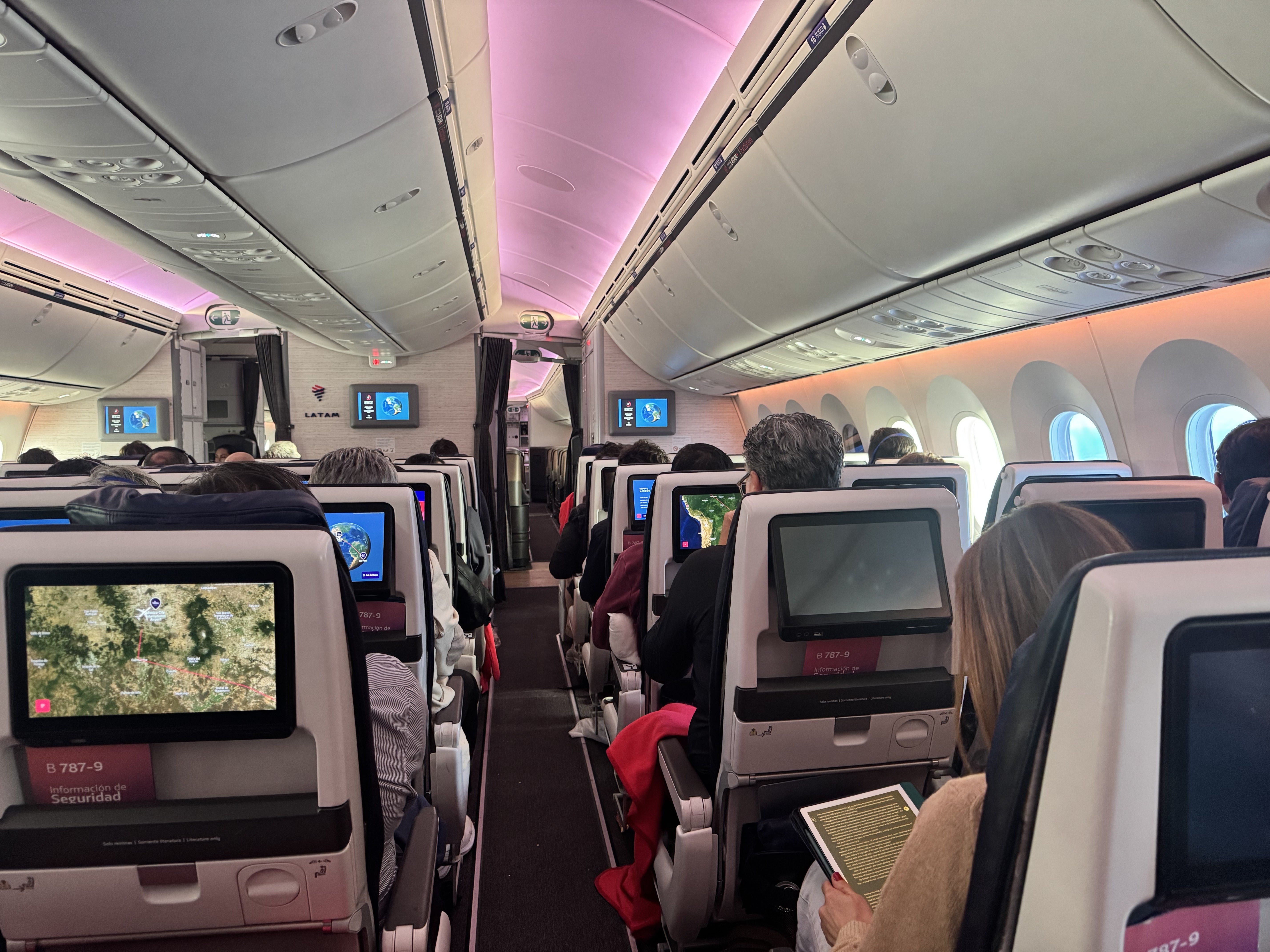 Boeing 787-9 economy cabin with rows of seats, overhead bins, and soft blue mood lighting along the aisle