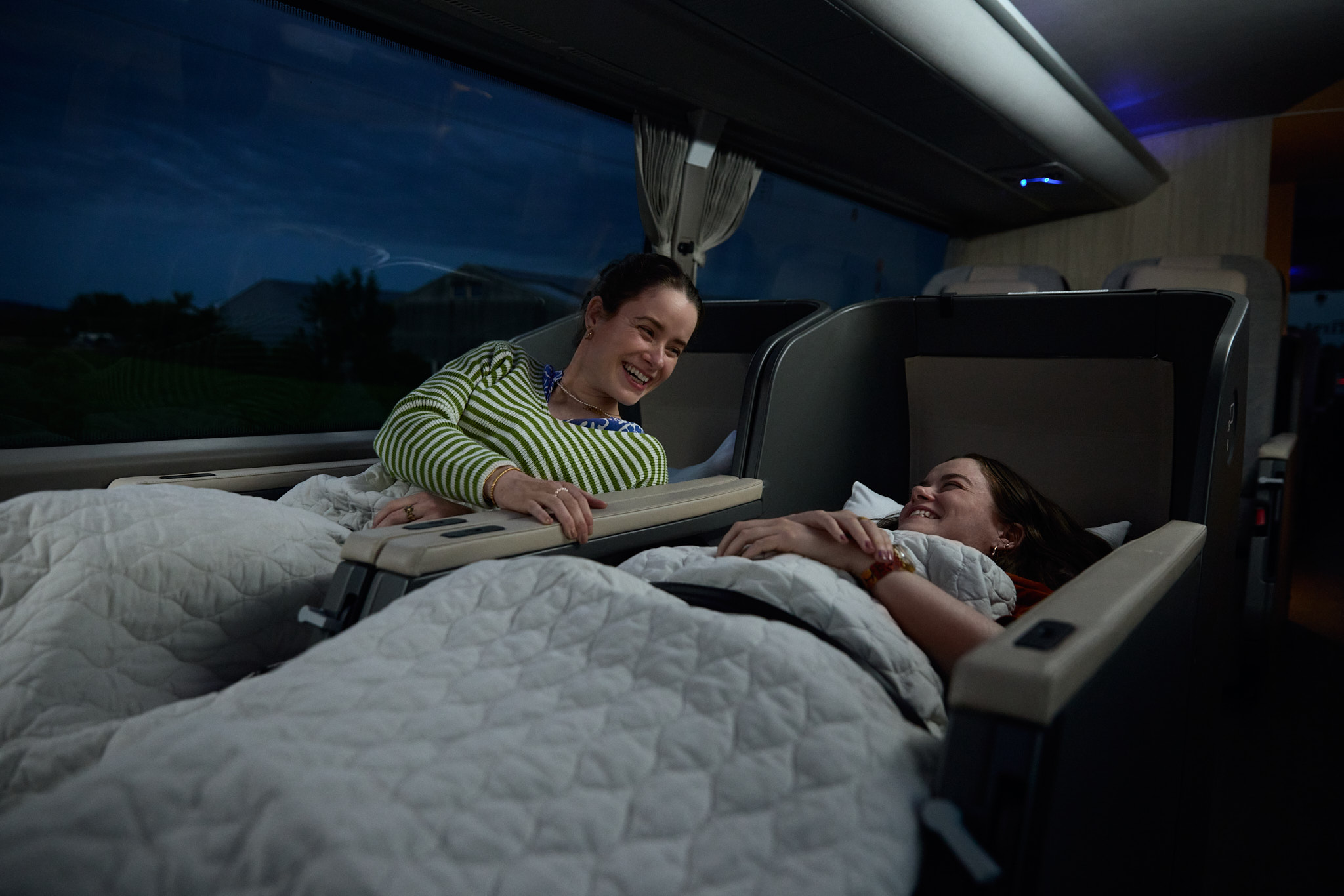 Interior of a Twiliner sleeper bus with lie-flat seats and dim nighttime cabin lighting