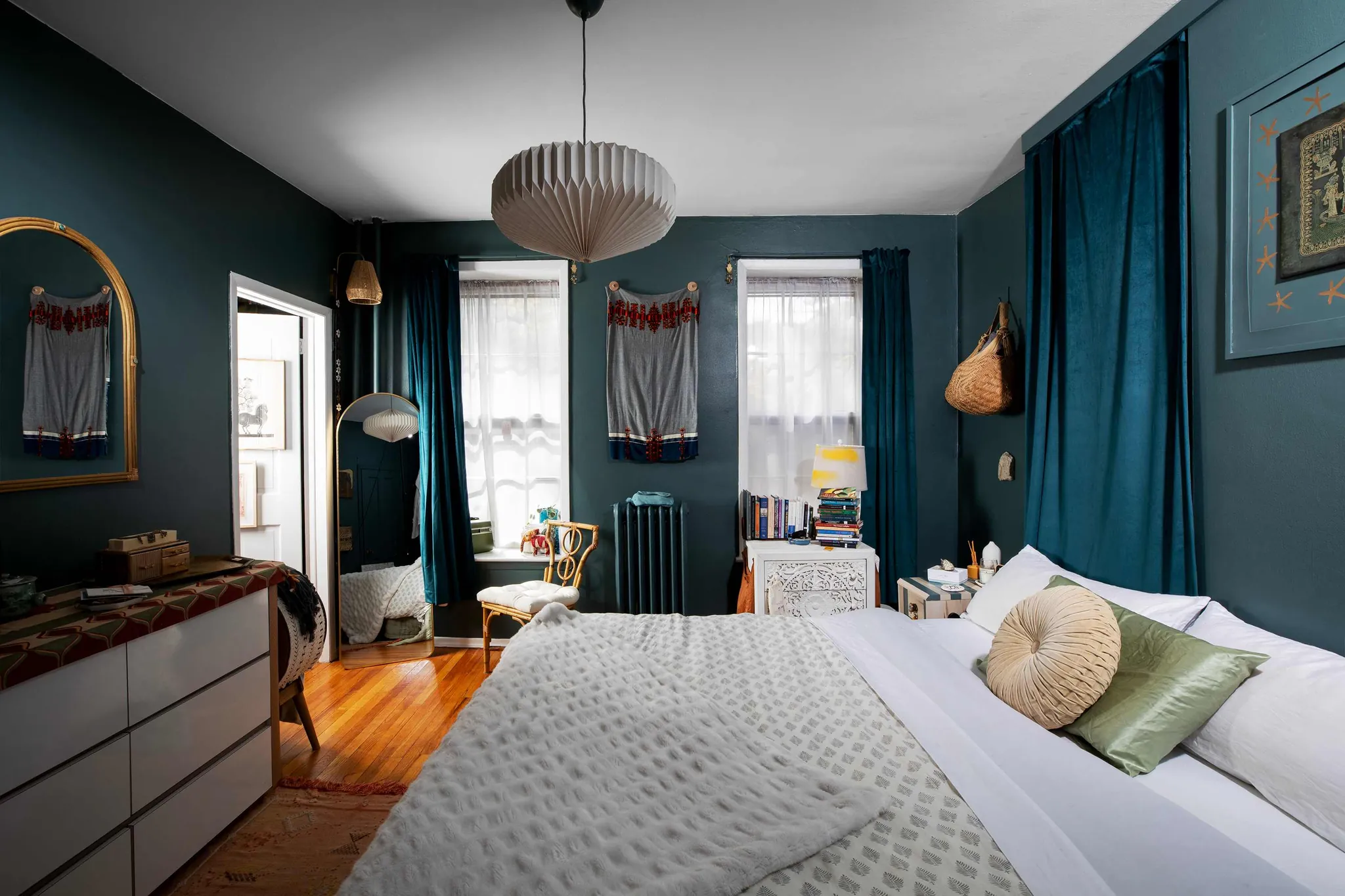 Bedroom with deep blue-grey Inchyra Blue walls, a wooden bed frame, neutral bedding, woven rug, and warm ambient lighting