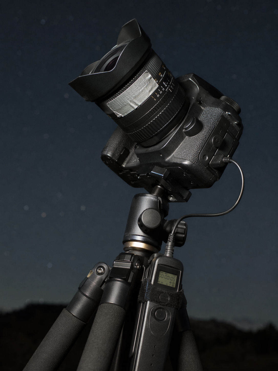 A DSLR with a wide-angle lens, connected intervalometer, and gaffer tape securing the focus ring