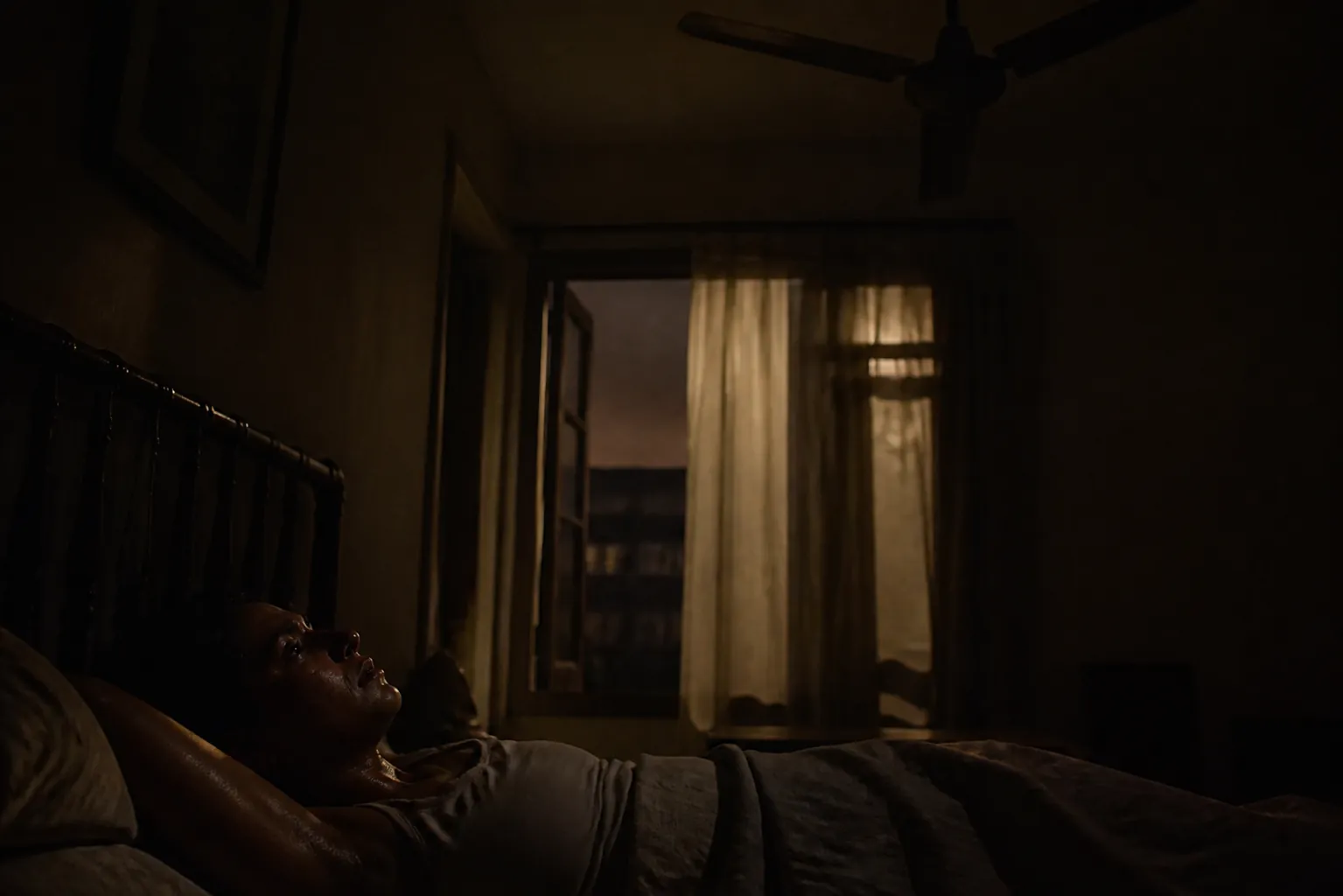 Dark bedroom during a heat wave blackout with a motionless ceiling fan above a restless sleeper