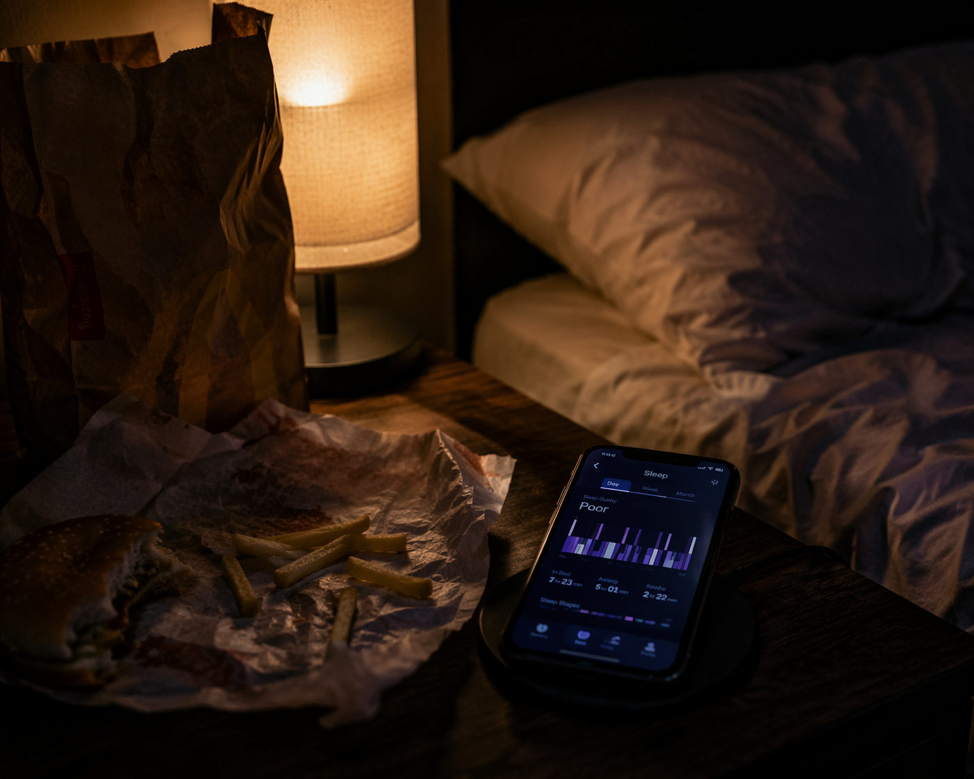 Half-eaten fast food beside a phone showing fragmented sleep in a dim bedroom