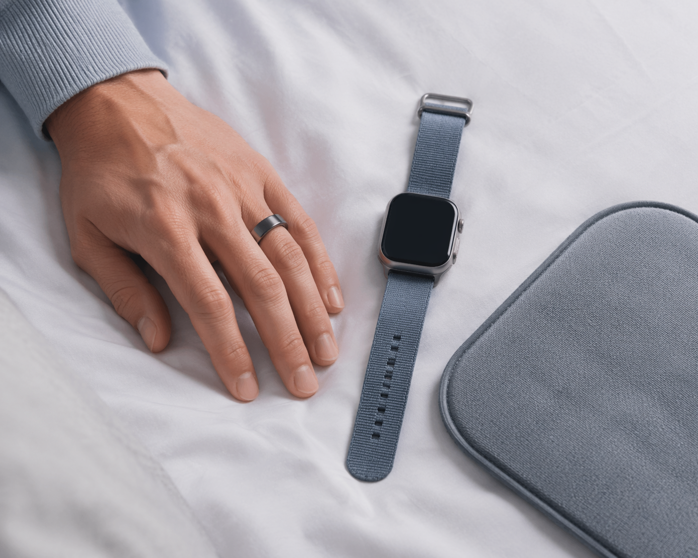 Smart ring, smartwatch, and sleep tracking mat arranged on white bedding