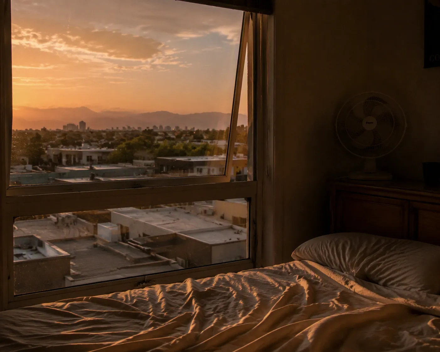 Denver apartment bedroom at twilight with a small fan, light sheets, and a hazy Front Range view