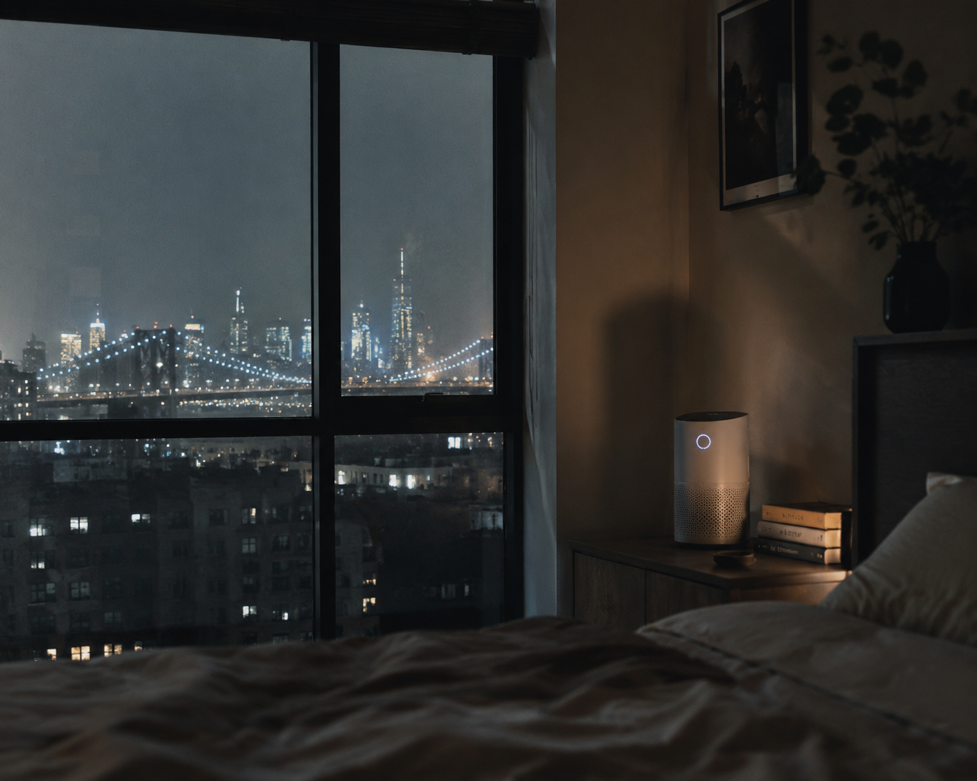 A dim NYC bedroom at night with a hazy skyline outside the window and a compact air purifier on the nightstand
