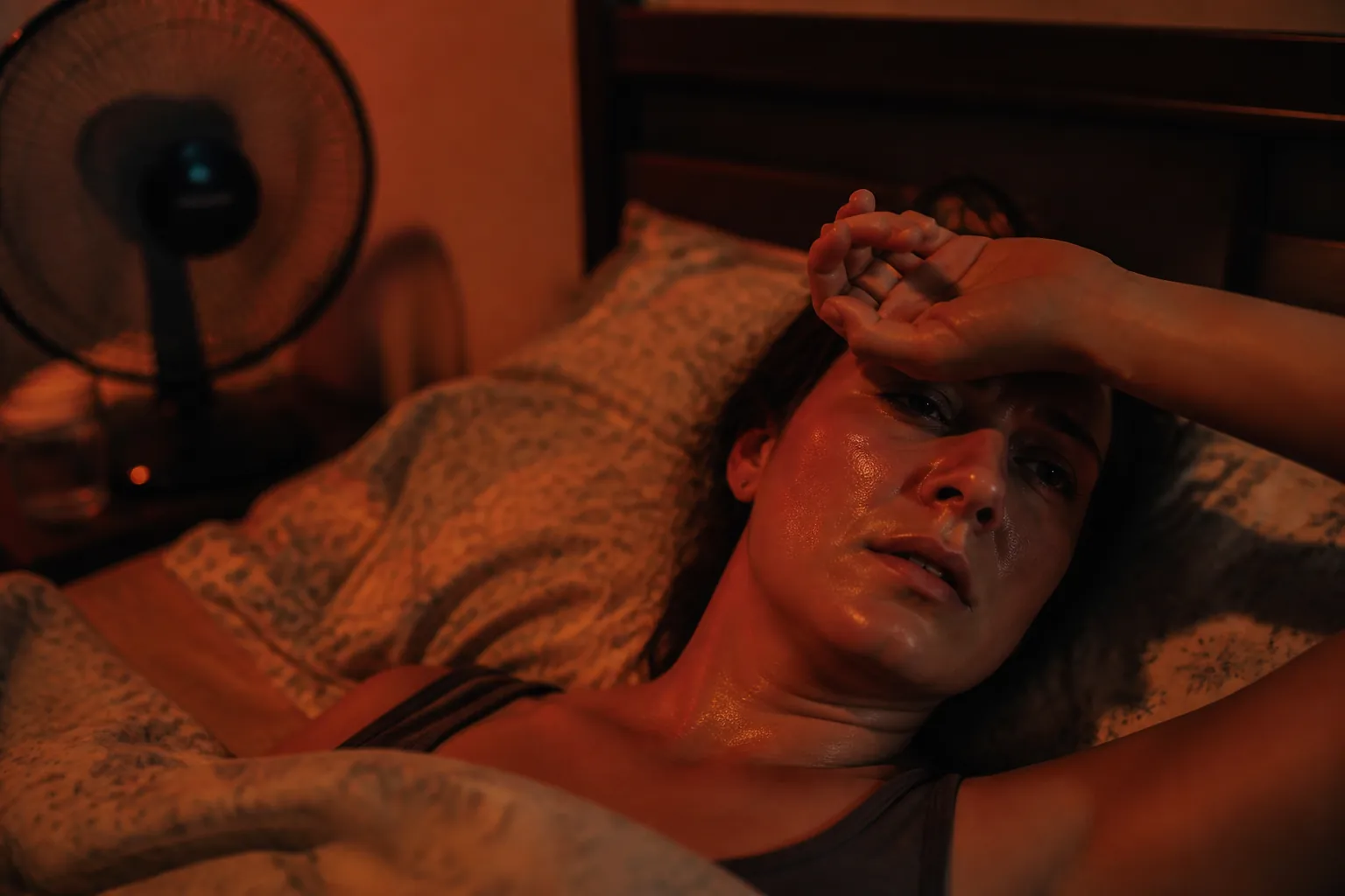 Person lying awake in bed during a heat wave with a fan nearby