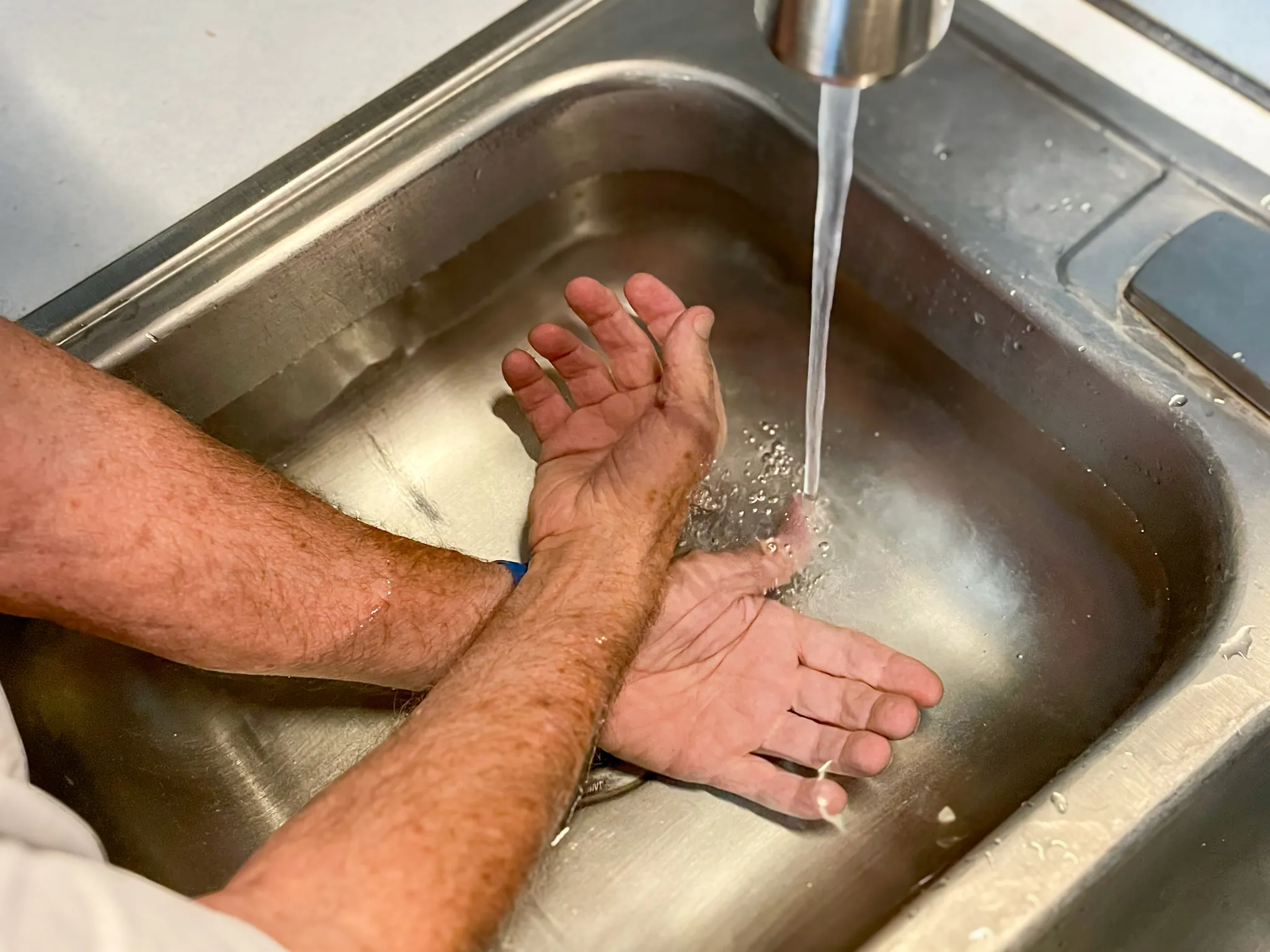 Older adult cooling both forearms in a basin of cool water