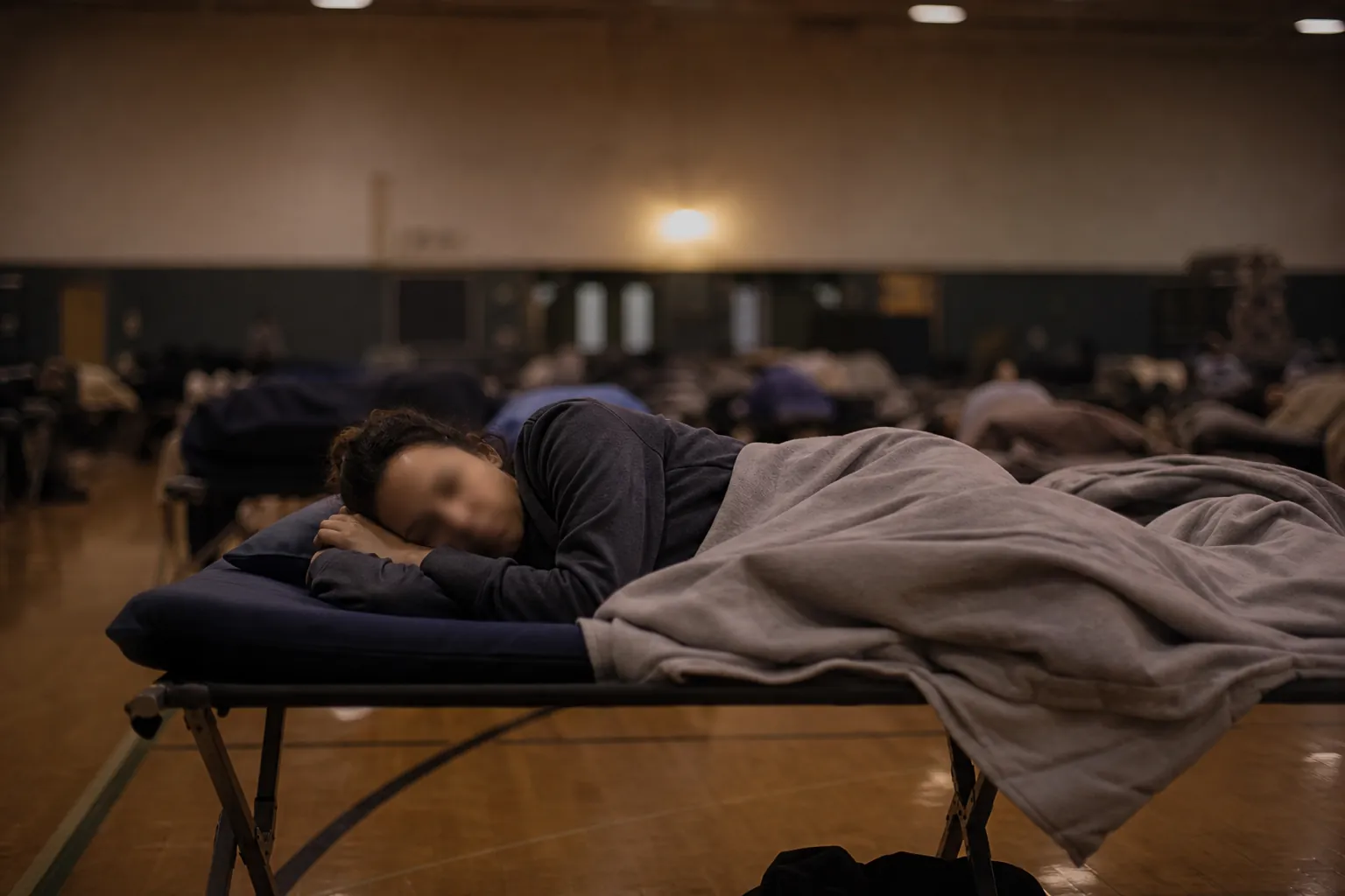 A person lying awake on a cot in a dim emergency shelter at night