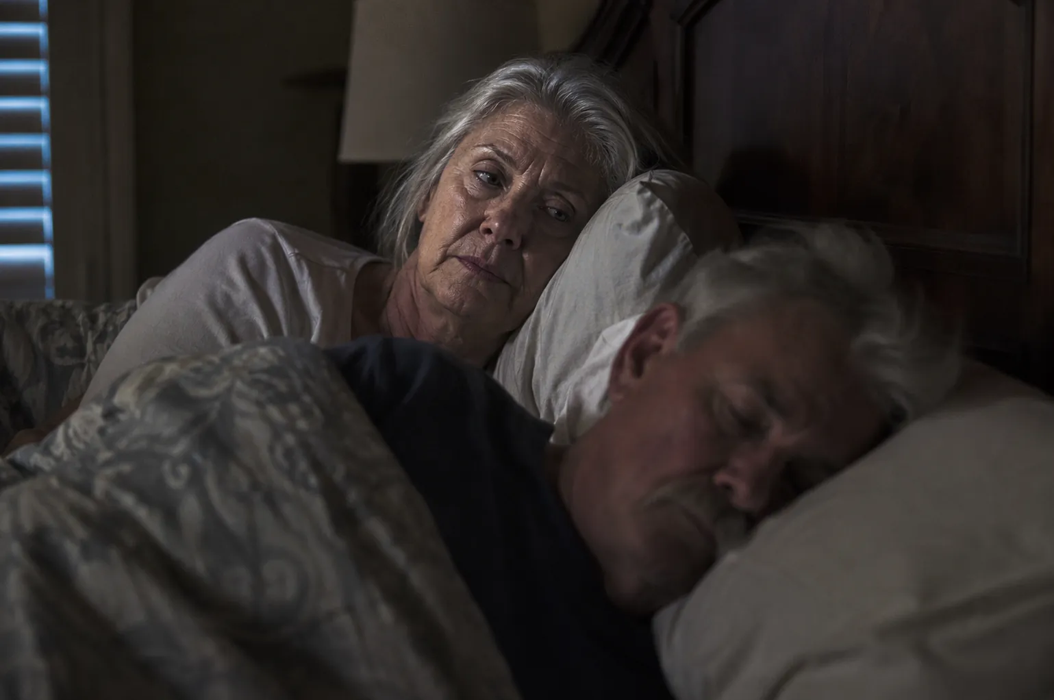 Older woman lying awake beside a restless sleeping partner