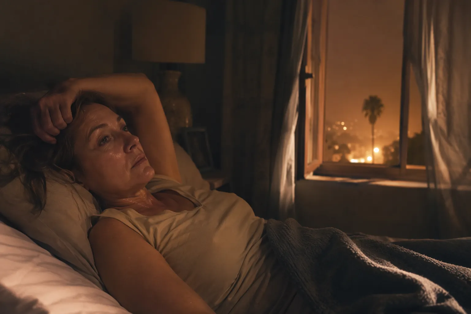 A middle-aged woman awake and overheated in a dim bedroom on a warm winter night